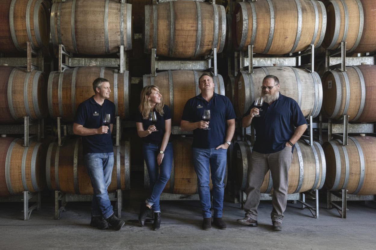 Four people standing in front of wine barrels in a winery setting